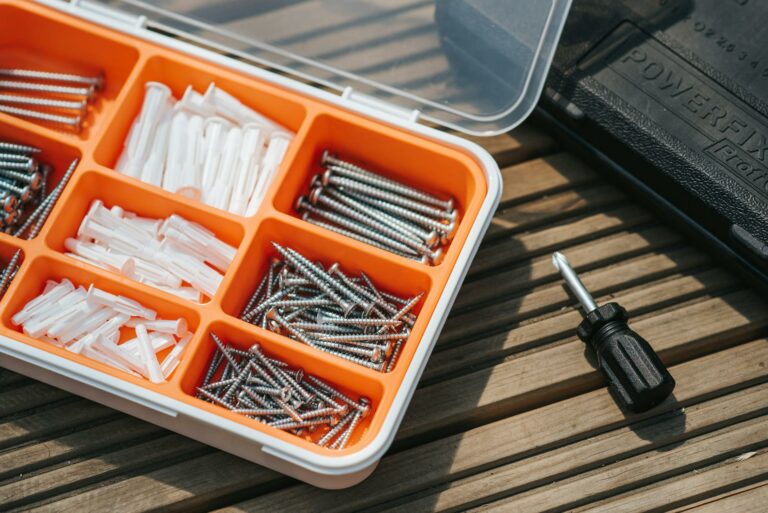 From above of container with assorted instruments placed on wooden surface near screwdriver and black case on street in sunlight